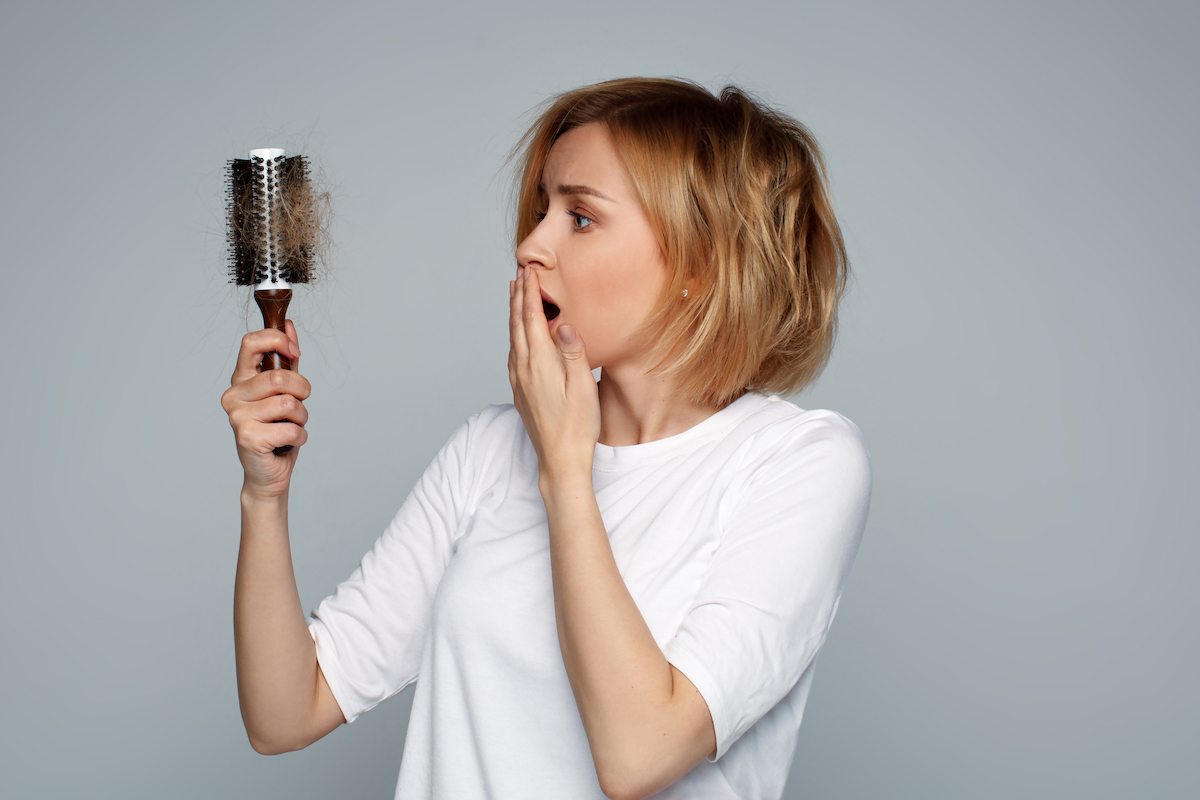 A young woman with short blonde hair looking nervously at her hair brush with a lot of hair in it.