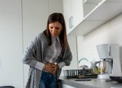 A woman holding her stomach in pain in the kitchen