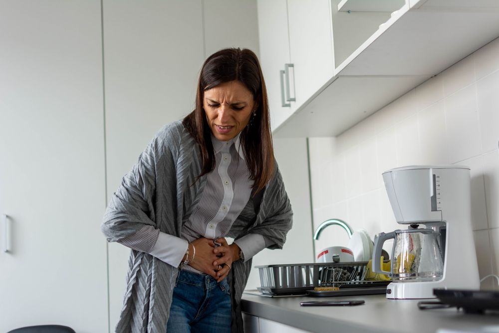 A woman holding her stomach in pain in the kitchen