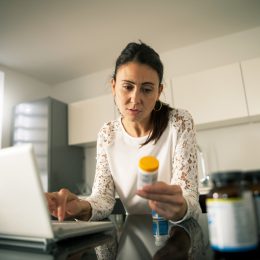 A woman sitting at her laptop and looking at a prescription pill bottle
