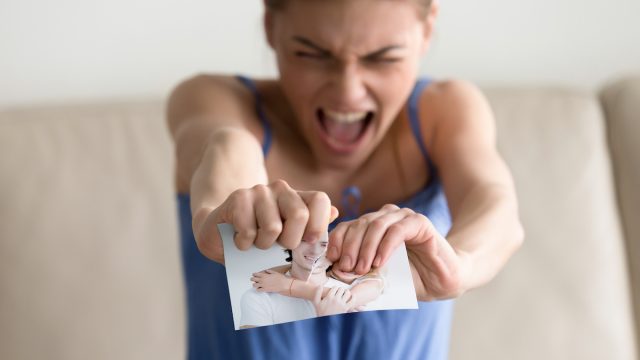 An angry woman tearing up a photo of a happy couple.