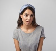Funny emotional young Caucasian woman wearing gray top and headscarf grimacing, rolling her eyes, expressing annoyance