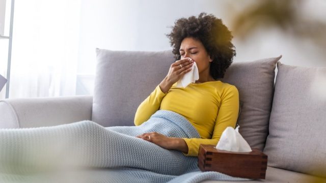 A woman blowing her nose while sick on the couch