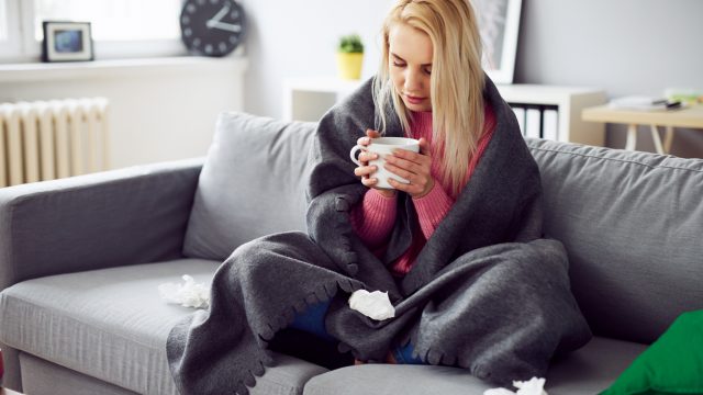 A young woman sitting on the couch with a mug while feeling sick