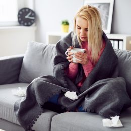 A young woman sitting on the couch with a mug while feeling sick