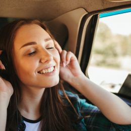 A toung woman traveling by car listening to music on wireless headphones.