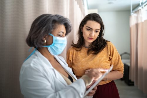 Doctor talking to patient during medical appointment in a hospital - wearing protective face mask