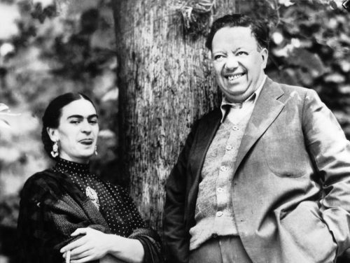 Frida Kahlo and Diego Rivera laugh together in a black and white photo.