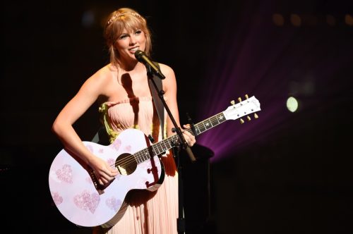 Taylor Swift performing on stage and playing a pink guitar. 