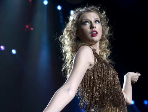 Taylor Swift wearing a gold sequined dress performing on tour. 