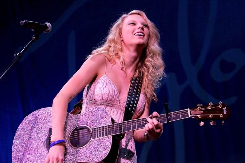 Taylor Swift performing on stage and playing guitar. 