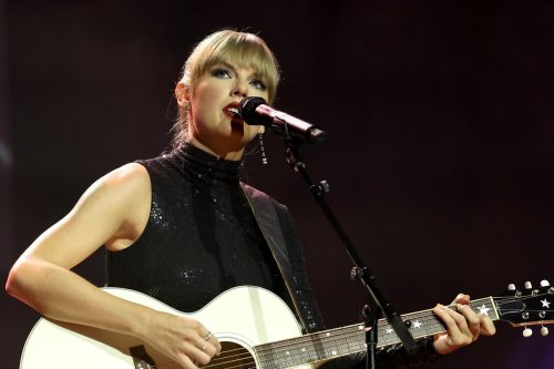 Taylor Swift performing in a black dress playing guitar.