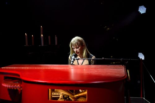 Taylor Swift sings and plays a red piano. 