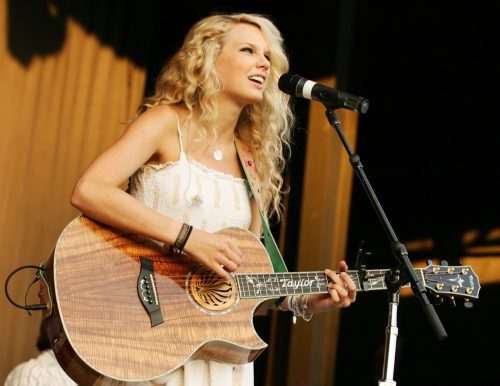 Taylor Swift in 2007 wearing a white dress, performing with a brown guitar. 