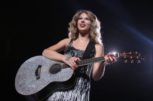 Taylor Swift wearing a silver dress performing on stage.