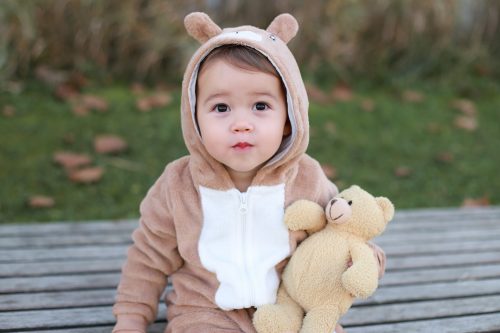 baby boy in a bear onesie holding a teddy bear