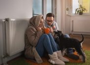couple and dog sit by radiator trying to stay warm