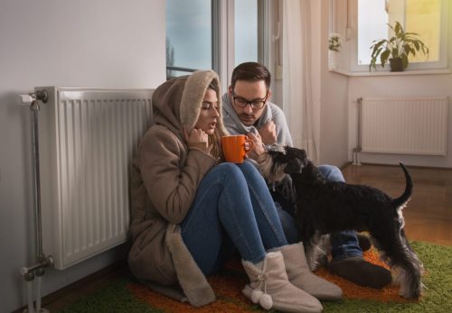 couple and dog sit by radiator trying to stay warm