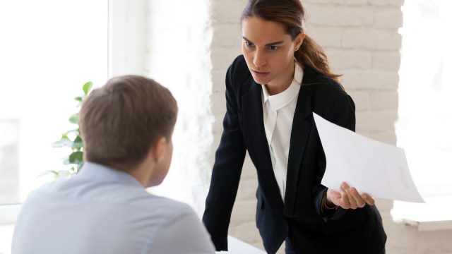 Serious businesswoman blaming employee for mistake in paper document