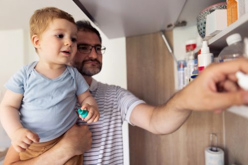 mature adult father and his baby son taking medicines out of medicine cabinet at home.