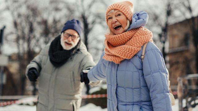 Excited aged woman pulling hand of her husband and smiling