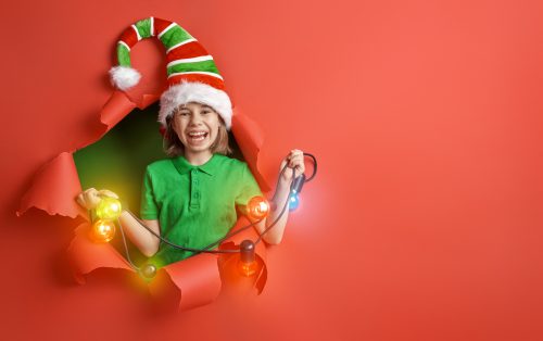 little girl dressed up as an elf draped in Christmas lights