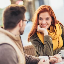 A couple sitting at an outdoor cafe; the woman is smiling and staring at her partner.