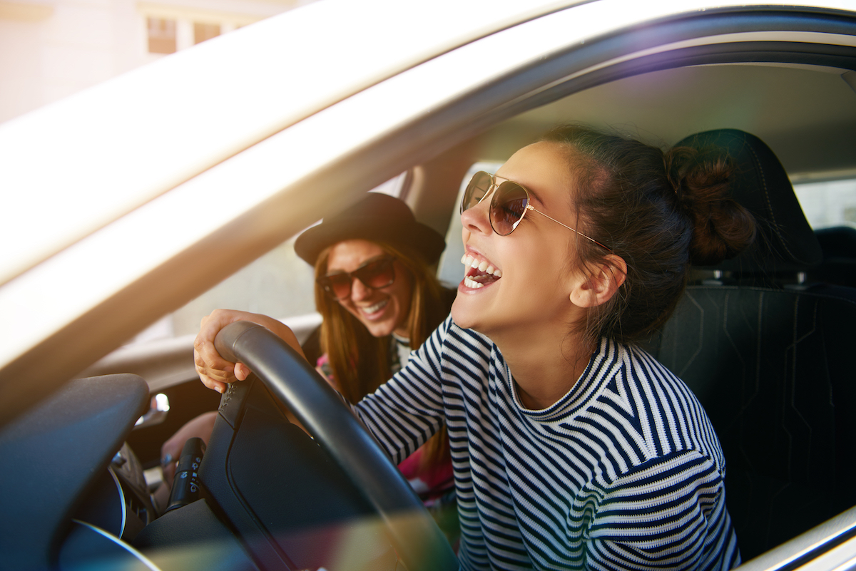 Laughing young woman wearing sunglasses driving a car with her girl friend