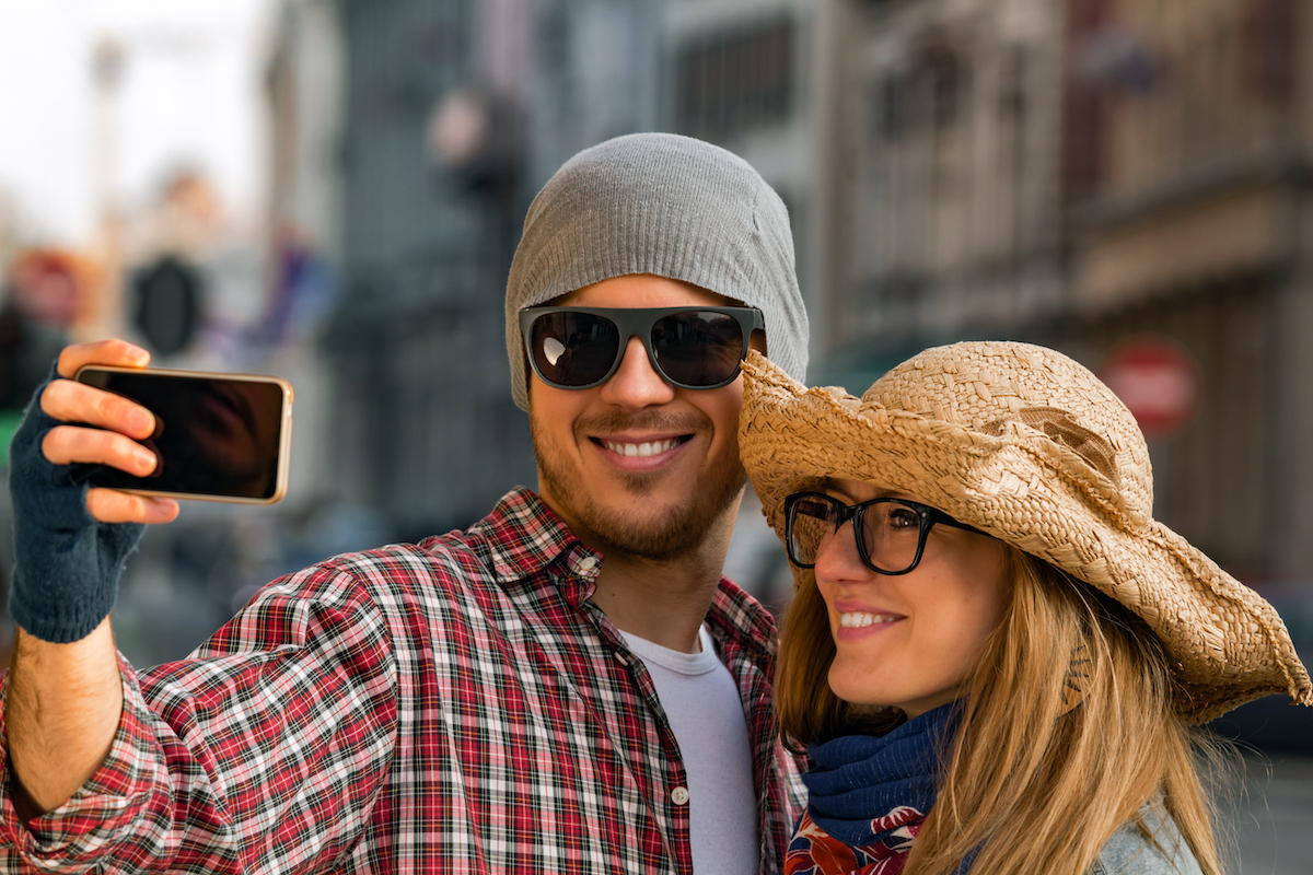 A young tourist couple wearing hats and taking a selfie.