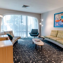 A retro-themed hotel suite with mid century modern couch, able, chair, and painting