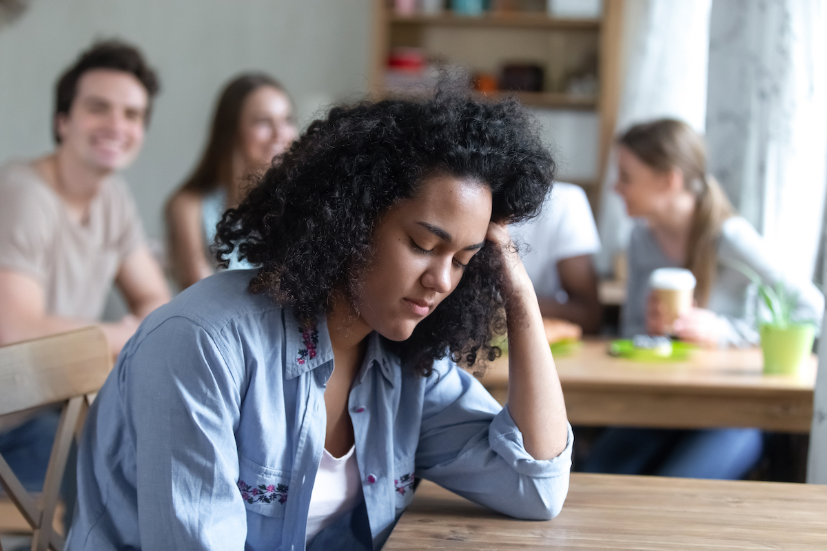A sad young woman sitting separately from her peers.