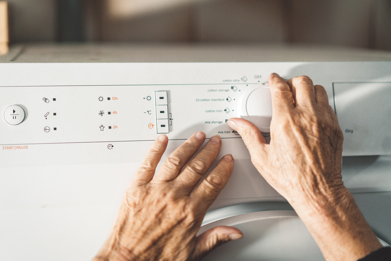 Hands touching the controls of a washer or dryer machine. 