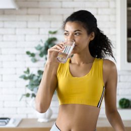 Woman standing in her kitchen drinking water.