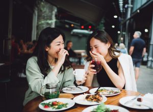 two asian women laughing and eating lunch together