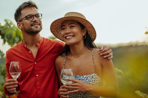 Diverse couple enjoying a glass of wine while walking through the vineyard