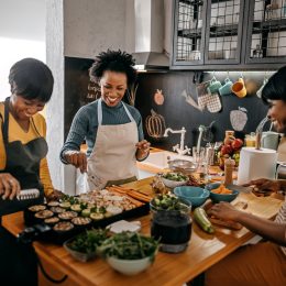 three black woman laughing and preparing dinner together