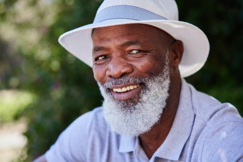Portrait of a smiling mature African man sitting alone at a table outside on a sunny afternoon in the summertime