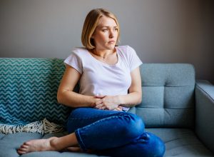 Woman sitting on sofa with stomach pain.