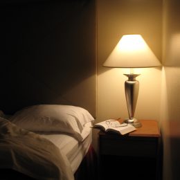 Bed next to night table with a lamp turned on.