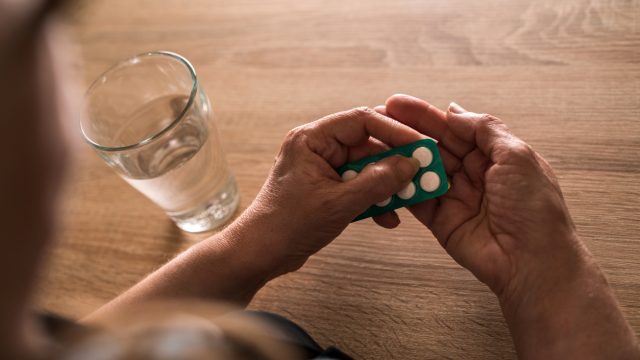 Woman's hands holding pills next to a glass of water on a table.