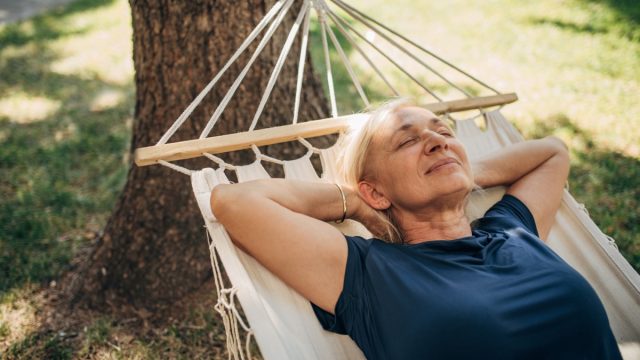 one woman, mature female lying in a hammock alone in back yard.