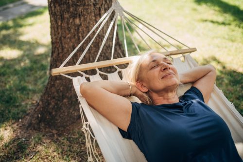 one woman, mature female lying in a hammock alone in back yard.