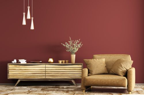 Modern interior of living room with wooden dresser and brown armchair over red wall