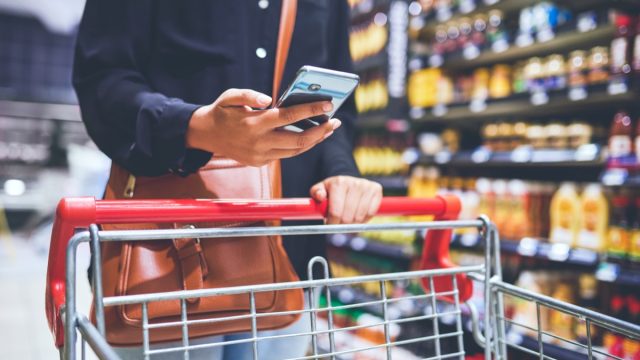 Cropped shot of a woman using a smartphone while shopping in a grocery store