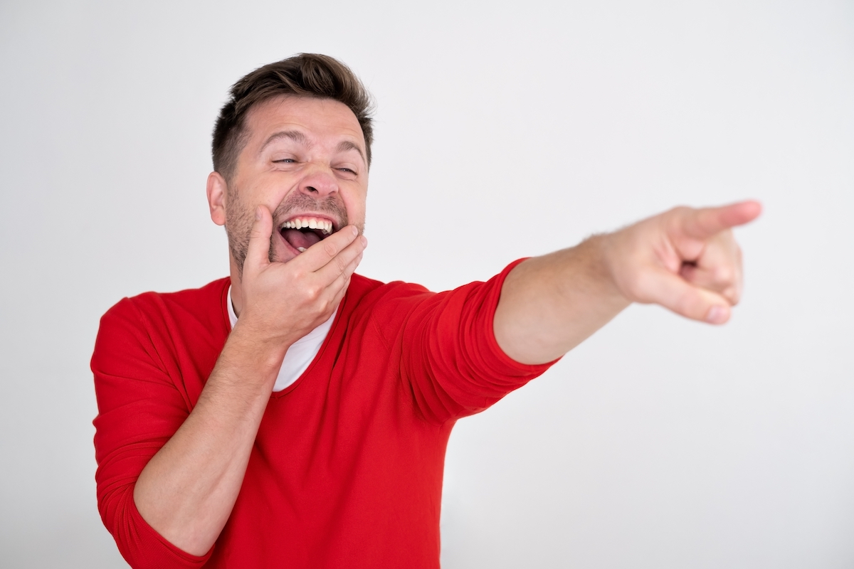 Man in a red sweater laughing and pointing at something.