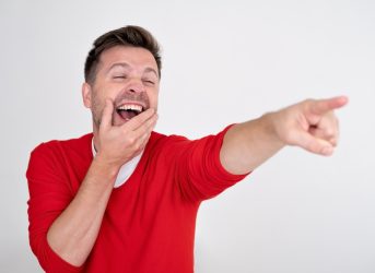 Man in a red sweater laughing and pointing at something.