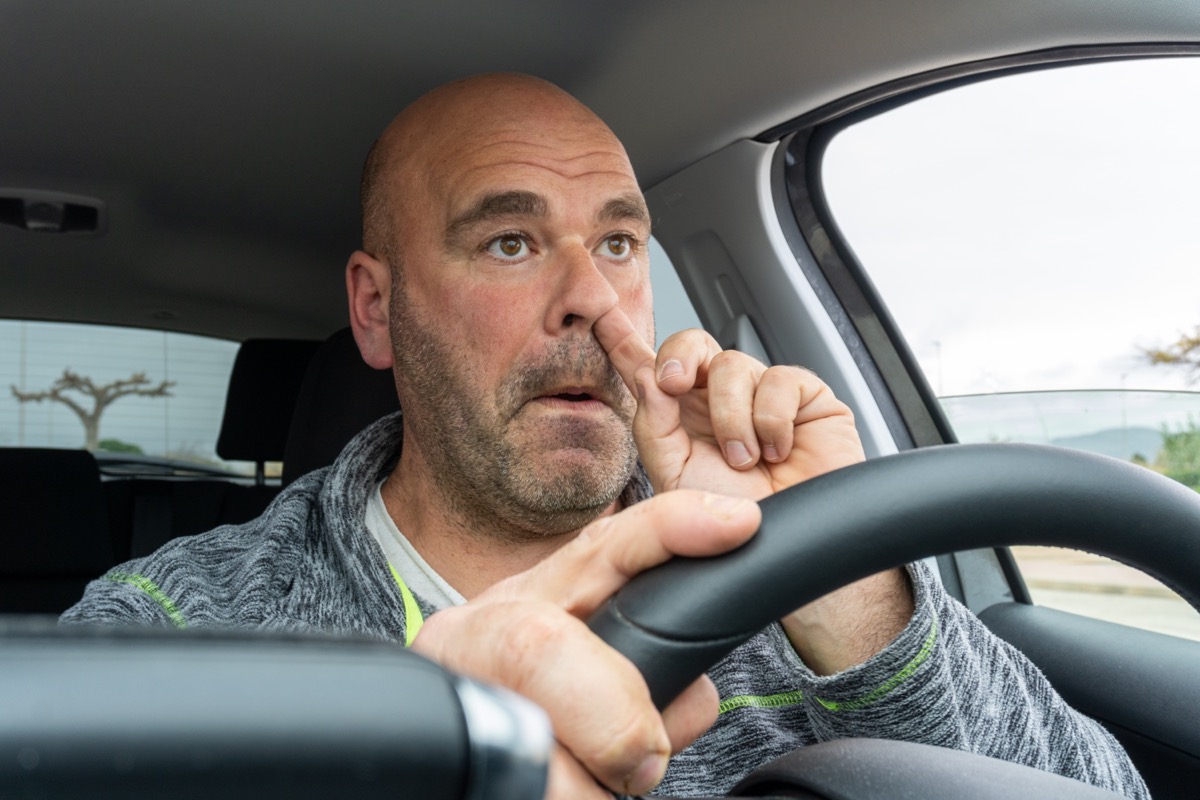 Middle-aged man picking his nose while driving a car.
