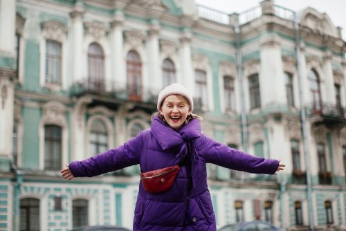 Woman in purple long down coat with arms out wide smiling