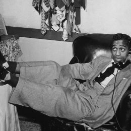 Sammy Davis Jr. photographed lounging in a chair, holding a phone circa 1955