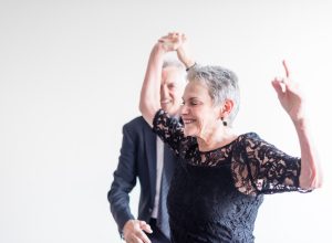 Close up of elegantly dressed older man and woman dancing exuberantly against neutral background